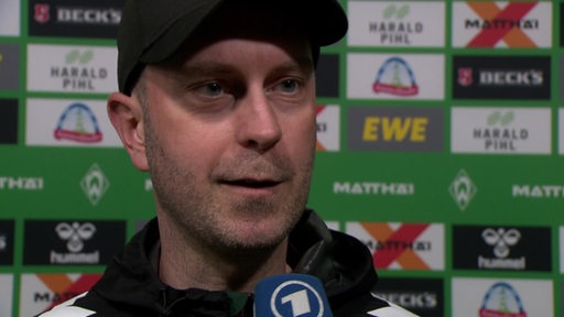 Werder-Trainer Ole Werner steht nach dem Spiel gegen Leipzig vor einer Werbewand beim Interview.