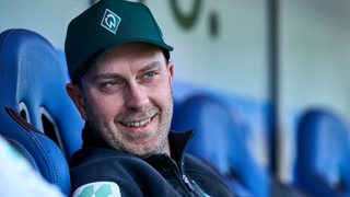 Werder-Trainer Ole Werner sitzt entspannt und lächelnd beim Testspiel gegen Meppen auf der Trainerbank.