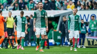 Werder-Spieler um Kapitän Marco Friedl stehen nach der Niederlage gegen Wolfsburg konsterniert auf dem Spielfeld.