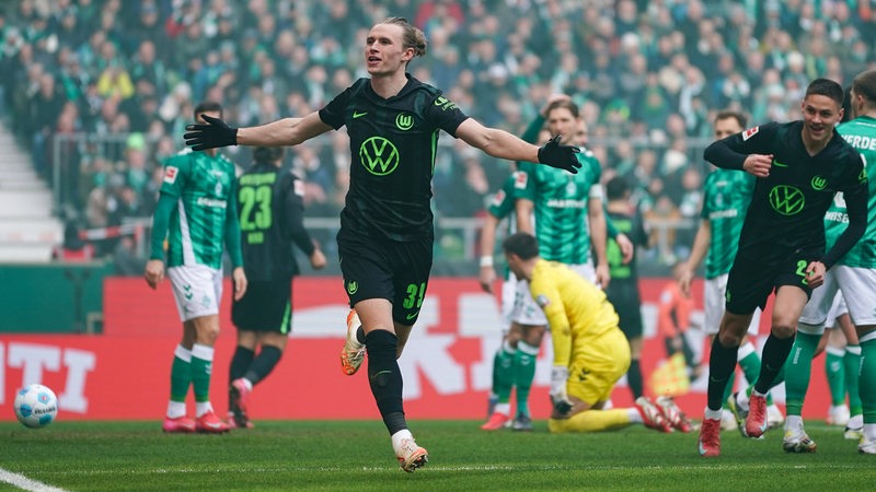 Wolfsburgs Profi Patrick Wimmer breitet nach seinem Tor jubelnd die Arme aus, hinter ihm die konsternierten Werder-Spieler und der düpierte Torwart Michael Zetterer, der auf dem Boden kniet.