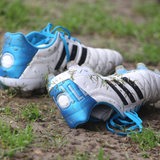Dreckige Fußballschuhe in blau und weiß liegen auf dem Boden