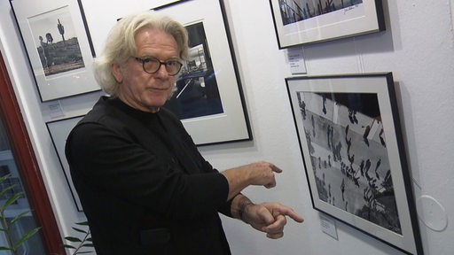 Ein Mann zeigt Fotografien in seiner Gallerie und erklärt. 