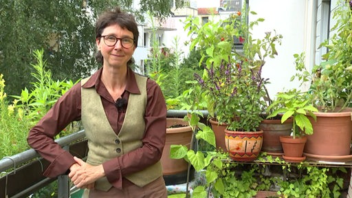 Die Supervisorin Susanne Fuchs steht zwischen mehreren grünen Pflanzen auf einem Balkon.