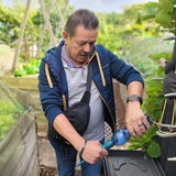 Ein Mann steht in einem Garten und hält eine Plastikflasche in der Hand.