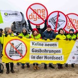 Menschen mit Banner protestieren am Strand gegen Gasbohrung