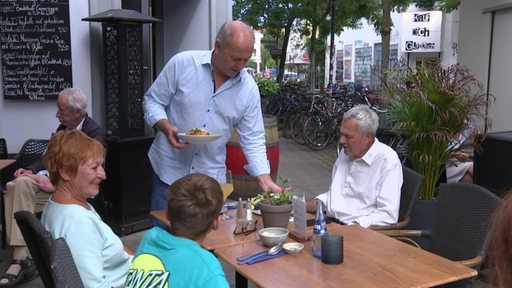 Der Restaurantbesitzer Andreas Hoetzel bringt Essen an einen Tisch. 