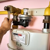 Hand dreht die Gasleitung an einem Gaszähler zu.