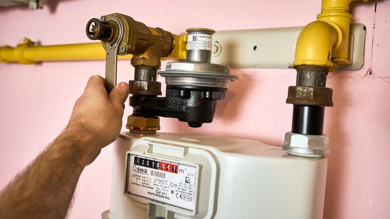 Hand dreht die Gasleitung an einem Gaszähler zu.