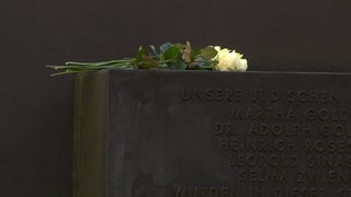 Der Gedenkstein der Rechspogromnacht in Bremen. Auf dem Gedenkstein liegen gelbe Rosen.