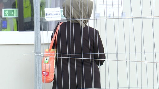 Eine Frau steht hinter einem Zaun vor einer Container-Notunterkunft für Geflüchtete