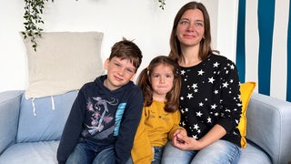 Eine Frau sitzt mit ihren zwei Kindern auf einer Couch.