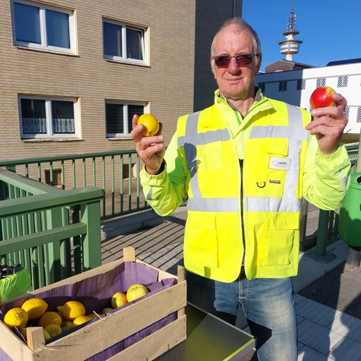 Ein Mann in Warnweste hält eine Zitrone und einen Apfel in den der Hand.