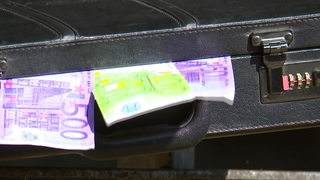 Mehrere Geldscheine hängen aus einem Koffer.