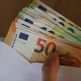 Eine Hand hält einen Briefumschlag voller 50- und 100-Euro-Scheine