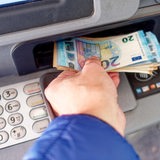 Eine Hand nimmt Geld aus einem Geldautomaten.