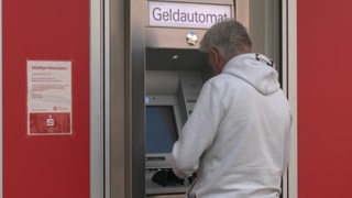 Ein roter Geldautomat, an dem ein Mann steht.