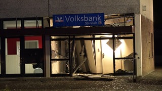 Blick auf die Bankfiliale von außen, Glasfront zerstört, Scherben liegen auf dem Boden, Inventar zerstört