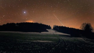 Geminiden-Sternschnuppen ziehen am Nachthimmel vorbei, Feld ist mit Schnee bedeckt