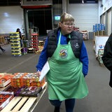 Eine Frau und ein Mann gehen durch eine Lagerhalle voller Gemüsekisten.