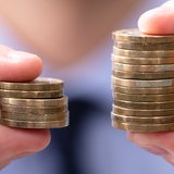 Hände halten zwei unterschiedlich große Stapel Euro-Münzen