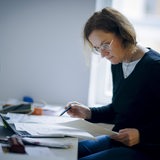 Eine Frau sitzt am Schreibtisch im Buero und liest in Unterlagen. 