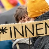 Auf einem Schild steht *innen, aufgenommen bei Demo gegen Söders Genderverbot. Im Hintergrund sind Demoteilnehmende zu sehen.
