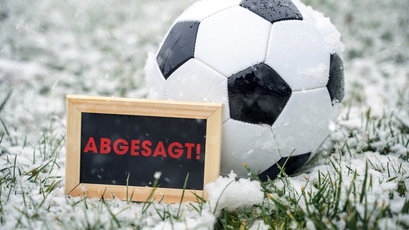 Im Schnee  liegt ein Fußball, davor in Schild mit der Aufschrift "Abgesagt"