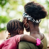 Rückenansicht einer afrikanischen jungen Frau mit einem Kind auf dem Arm.