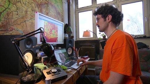 Geograf Julian Kraus sitzt am Schreibtisch, vor ihm Computer und Karten.