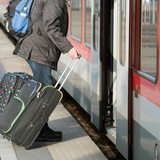 Ein Mann hat zwei Rollkoffer in der Hand und steigt in einen Zug ein