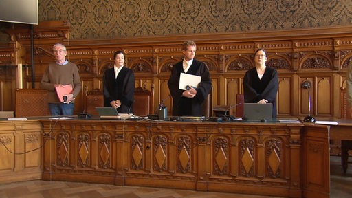 Mehrere Richter stehen hinter ihren Sitzplätzen im Gerichtssaal.
