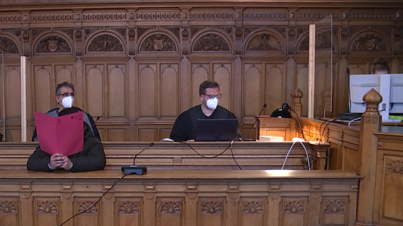 Ein Angeklagter sitzt in einem Bremer Gericht. Er hält sich einen Aktenordner vor das Gesicht.