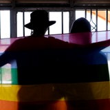 Silhouette eines schwules Paares, das sich mit einer Pride-Flagge bedeckt (Symbolbild)