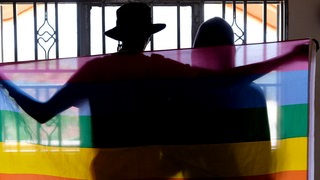 Silhouette eines schwules Paares, das sich mit einer Pride-Flagge bedeckt (Symbolbild)