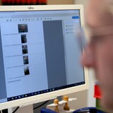 Ein Mann in Unschärfe vor einem Bildschirm mit verschiedenen Gesichtern und Personen.