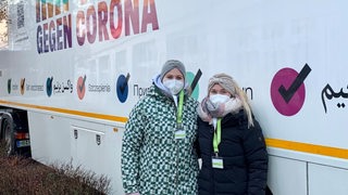 Zwei junge Gesundheitsfachkräfte stehen mit Masken vor einem Impftruck in Bremen-Nord
