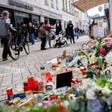 Zahlreiche Blumen und Kerzen stehen in einer Innenstadt an einer Hauswand.