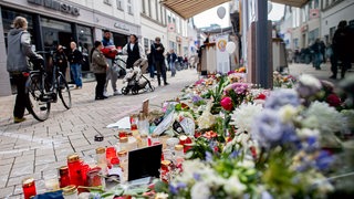 Zahlreiche Blumen und Kerzen stehen in einer Innenstadt an einer Hauswand.