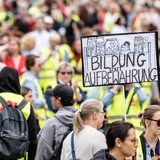 Menschen nehmen an einer Kundgebung der Gewerkschaften GEW und Verdi teil. Auf einem Schild ist die Aufschrift "Bildung statt Aufbewahrung" zu lesen.