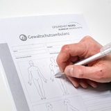 Eine Hand füllt ein Formular zur Dokumentation in der Gewaltschutzambulanz aus.