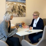 Zwei Frauen sitzen an einem Tisch und sprechen miteinander.