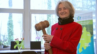 Barbara Stollberg lächelt und hält einen großen Hammer in den Händen.