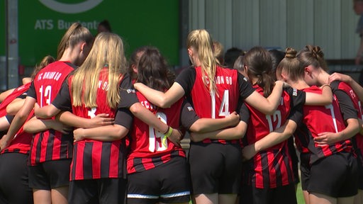 Mehrere junge Fußballspielerinnen stehen einem Kreis und stecken die Köpfe zusammen.