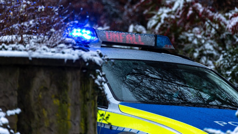 Ein Polizeiwagen mit Blaulicht und LED-Schrift vor verschneiter Landschaft. 