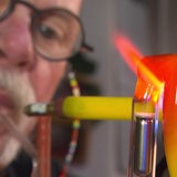 Ein Mann hat einen Schlauch im Mund, vor seinem Gesicht ein buntes Rohr aus Glas.