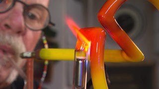 Ein Mann hat einen Schlauch im Mund, vor seinem Gesicht ein buntes Rohr aus Glas.