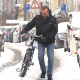 Ein Mann schiebt sein Fahrrad durch den Schnee.