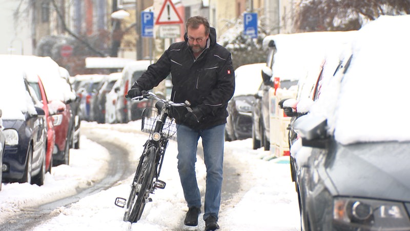 Ein Mann schiebt sein Fahrrad durch den Schnee.