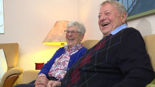 Ein Ehepaar lachend auf einer Couch.