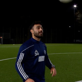 Ein Spieler im Trainingsanzug steht in der Dunkelheit auf einem Fußballplatz